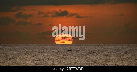 Petit bateau de pêche et le coucher du soleil, un petit bateau de pêche navigue alors que le Soleil descend derrière l’horizon. Photographie de paysage marin panoramique. Banque D'Images