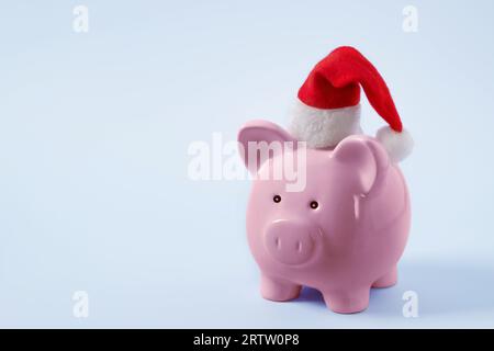 Économies de Noël ou concept de shopping. Tirelire rose dans un chapeau de Père Noël. Banque D'Images