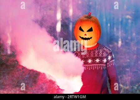 Portrait d'une personne adulte avec la citrouille d'Halloween sur la tête dans une nuit de bois avec de la fumée colorée. Halloween Jack-o-Lantern drôle fête. Banque D'Images