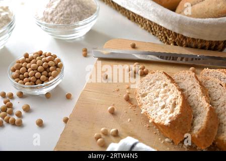 Pain de soja tranché sur une planche à découper sur un banc de cuisine avec des haricots de soja et de la farine. Vue surélevée. Banque D'Images