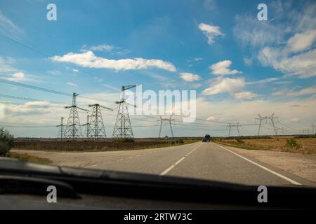 Tour de transmission d'énergie en Ukraine en été. Fils aériens des supports de ligne de transmission d'énergie haute tension à travers un champ, vue de l'intérieur de Banque D'Images
