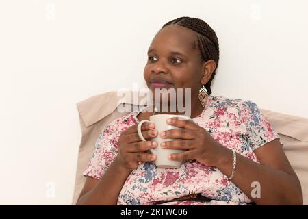 Portrait d'une jeune femme vêtue d'une robe florale rose se relaxant avec une tasse de thé Banque D'Images