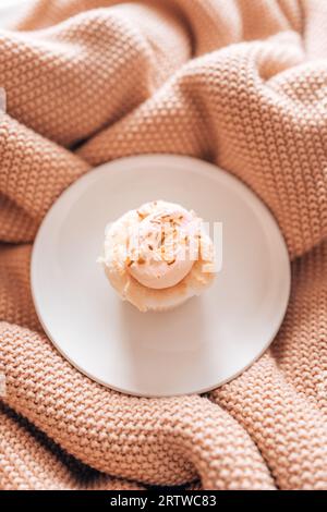 Un cupcake givré rose assis sur une assiette blanche sur une texture rose Banque D'Images