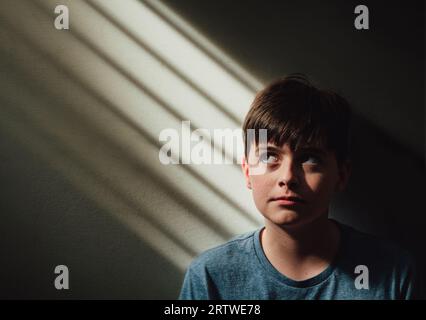 Gros plan portrait de garçon contre le mur dans la tache de soleil. Banque D'Images