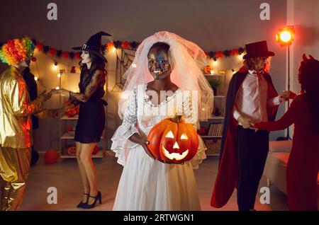 Heureuse femme noire habillée en mariée morte avec son jack-o-lanterne à la fête d'Halloween Banque D'Images