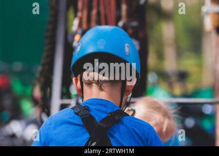 Vue sur le cours de cordes élevé, enfants de l'escalade dans le parc de corde d'activité d'amusement, obstacles de passage et tyrolienne sur les hauteurs, enfants adolescents en equipme Banque D'Images