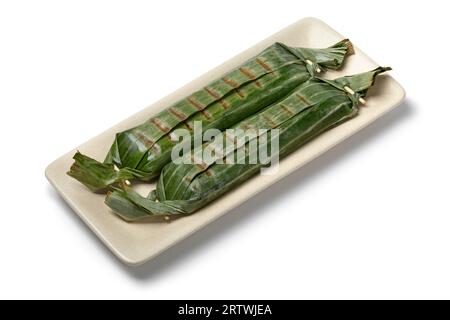 Lemper grillé frais enveloppé dans des feuilles de bananier, une collation savoureuse indonésienne faite de riz gluant farci en gros plan sur un plat, isolé sur fond blanc Banque D'Images