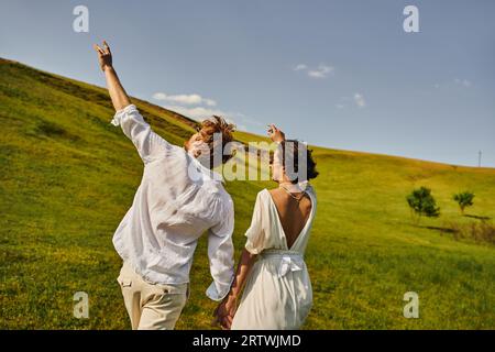 mariage rural, juste marié couple en robe de mariée tenant la main et marchant dans le champ vert Banque D'Images