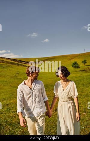 mariage à la campagne, couple multiethnique tenant la main dans le champ vert, juste mariés jeunes mariés Banque D'Images