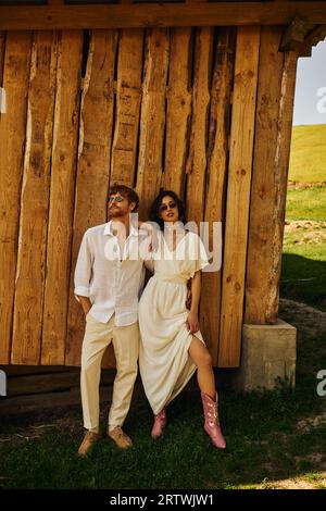 mariage rustique dans le style boho, mariée asiatique élégante en robe de mariée debout avec marié dans les lunettes de soleil Banque D'Images