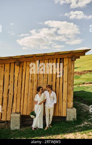 mariage rustique dans le style boho, mariée asiatique en robe de mariée et bottes de cow-boy debout avec marié Banque D'Images