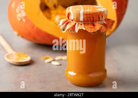 Bocal en verre avec confiture de citrouille d'orange maison en gros plan devant une citrouille fraîche Banque D'Images