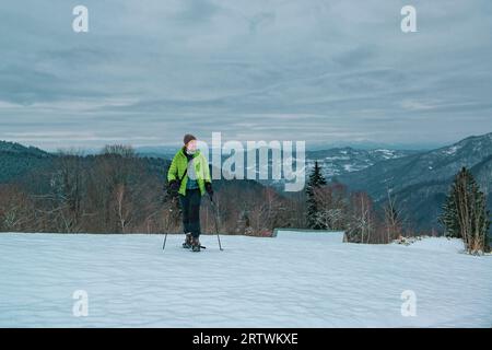 Homme randonneur solitaire avec des raquettes de neige et des bâtons de trekking marche sur le champ de neige haut dans les montagnes d'hiver Banque D'Images