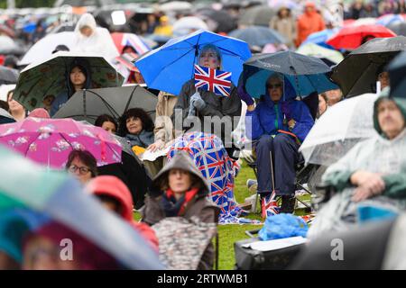 Une femme qui se réfugie de la pluie sous un parapluie tient un drapeau de l'Union Jack. Elle fait partie d'une grande foule de gens qui regardent le couronnement du roi CH Banque D'Images