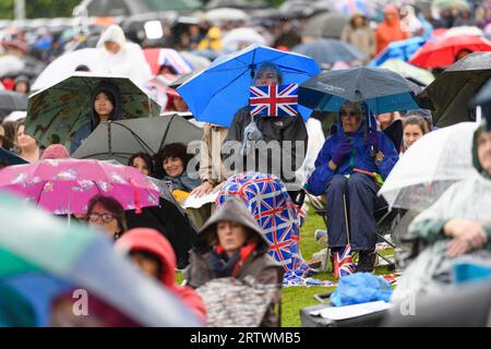 Une femme qui se réfugie de la pluie sous un parapluie tient un drapeau de l'Union Jack. Elle fait partie d'une grande foule de gens qui regardent le couronnement du roi CH Banque D'Images