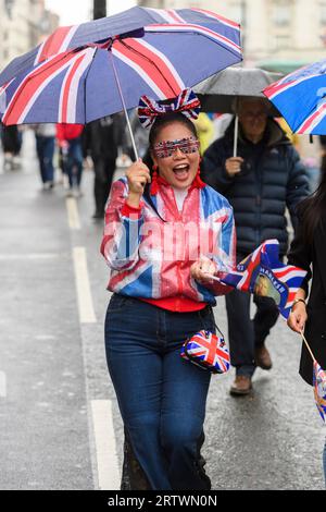 Une femme, vêtue d'une veste Union Jack, et des lunettes, et portant un parapluie et un sac assortis, descend un Piccadilly pluvieux, partie d'une grande foule h Banque D'Images