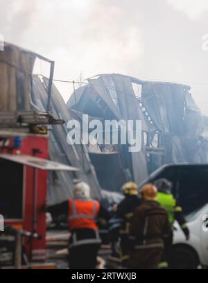 Grand incendie de flamme massive dans la ville, usine d'entrepôt flamboyante, bâtiment de stockage brûle, équipe de pompiers éteignant le feu, pompiers en service, Banque D'Images