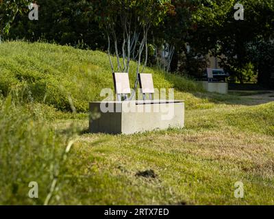 Deux sièges vides dans un parc public. Banc en ciment et bois au soleil pendant la journée. L'herbe est verte et coupée. Banque D'Images