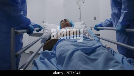 Les chirurgiens transportent le patient senior dans le couloir de la clinique jusqu'à la salle d'opération. Les médecins ouvrent des portes pour d'autres médecins avec le patient. Vieil homme allongé sur la civière sous goutte et avec un oxymètre de pouls sur son doigt. Banque D'Images