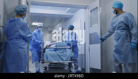 L'infirmière et le personnel paramédical ouvrent les portes des couloirs de l'établissement médical. Les chirurgiens multiethniques poussent la civière avec le patient âgé couché à la salle d'opération. Le personnel médical travaille aux urgences. Ralenti. Banque D'Images