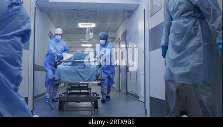 L'infirmière et le personnel paramédical ouvrent les portes des couloirs de l'établissement médical. Les chirurgiens multiethniques poussent la civière avec le patient âgé couché à la salle d'opération. Le personnel médical travaille aux urgences. Ralenti. Banque D'Images