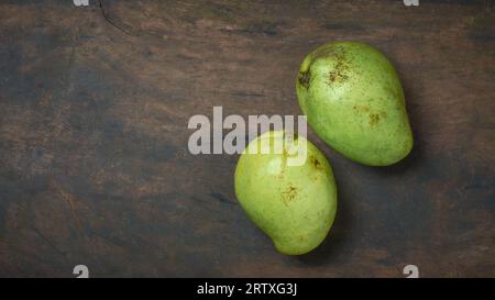 deux mangues sur un plateau de table rustique en bois, mangifera indica, fruit tropical populaire originaire d'asie du sud et connu pour ses délicieusement sucrés et juteux Banque D'Images