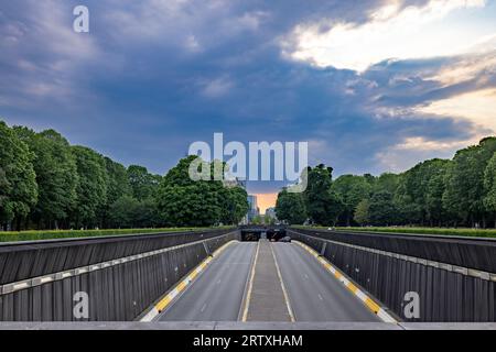 Parcourez une route moins empruntée car elle disparaît dans les profondeurs d'un tunnel. Flanqué par la beauté sereine de la nature, de grands arbres bordent le chemin, vous invitant à vous aventurer. Mais méfiez-vous, car alors que le soleil se couche et que les nuages se rassemblent, une aventure orageuse attend.Road to the Unknown : tunneling dans Stormy Skies. Photo de haute qualité Banque D'Images