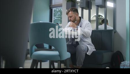 Médecin professionnel utilise la tablette numérique dans le café de la clinique moderne pendant la pause. Medic mange le dîner, regarde les résultats des tests médicaux du patient ou surfe sur Internet. Le personnel médical en salle à manger hospitalière. Banque D'Images