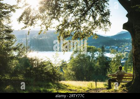 Homme sur un banc profite du soleil du soir à Titisee dans la Forêt Noire, Baden-Wuerttemberg, Allemagne Banque D'Images