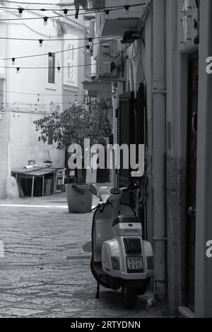 Vicolo della città vecchia di Bari che conduce alla strada delle orecchiette (Arco Basso). Veduta delle case con vespa parcheggiata e luci appese Banque D'Images