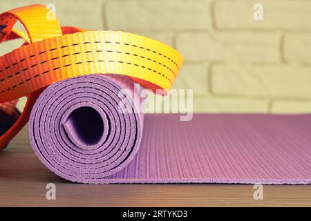 Tapis de fitness violet et rubans de ceinture orange sur le plancher en bois dans le studio de gym. Exercices et modèle d'activité sportive Banque D'Images