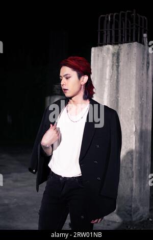 un asiatique aux cheveux rouges portant un t-shirt blanc et un costume noir dans un vieux bâtiment la nuit Banque D'Images