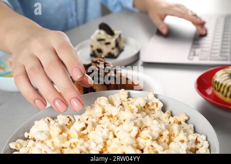 Mauvaises habitudes. Femme mangeant du pop-corn tout en utilisant un ordinateur portable à table, gros plan Banque D'Images