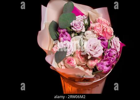 Bouquet de fleurs fraîches de différentes couleurs de roses dans un emballage en papier dans un vase sur le fond noir. Banque D'Images