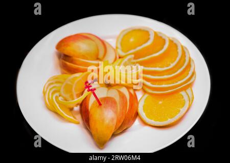 Assiette de fruits fruits agrumes frais sains tranches de pomme, citron et orange sur le fond noir isolé. Banque D'Images