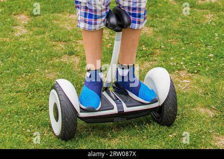 Les pieds d'un garçon en baskets se tiennent sur un hoverboard en gros plan sur le fond d'herbe dans le parc. Banque D'Images