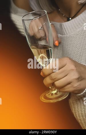 Gros plan de la main d'une femme adulte tenant un verre d'alcool de champagne pétillant frais sur un fond orange. Banque D'Images