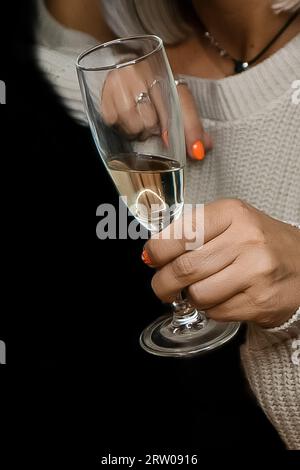 Gros plan de la main d'une femme adulte tenant un verre d'alcool de champagne mousseux frais sur un fond noir. Banque D'Images