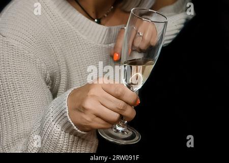 Gros plan de la main d'une femme adulte tenant un verre d'alcool de champagne mousseux frais sur un fond noir. Banque D'Images