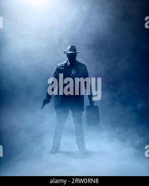Faceles homme avec une arme et une mallette debout dans le brouillard Banque D'Images
