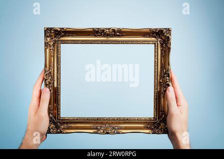 Homme tenant un cadre d'image doré look antique dans ses mains Banque D'Images