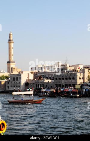 Vue sur la crique de Dubaï de Deira à Bur Dubai. Abras, les bateaux-taxis typiques de Dubaï, roulent sur la rivière. Le minaret de la Grande Mosquée Banque D'Images