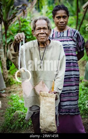 Sara village, Mt. Michael, Papouasie-Nouvelle-Guinée, juillet 2015 : un vieil homme autochtone tient un collier fait de perles et d'os et pose avec une jeune femme souriante Banque D'Images