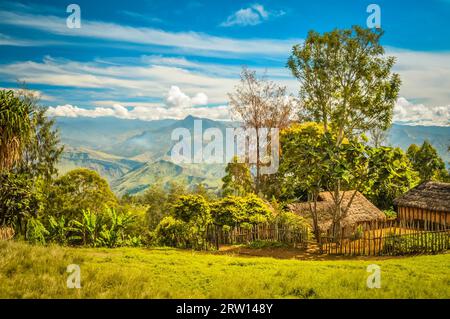 Photo de maison de village avec clôture en bois et de hautes montagnes au loin dans le village de Sara et Mt. Michael en Papouasie-Nouvelle-Guinée Banque D'Images