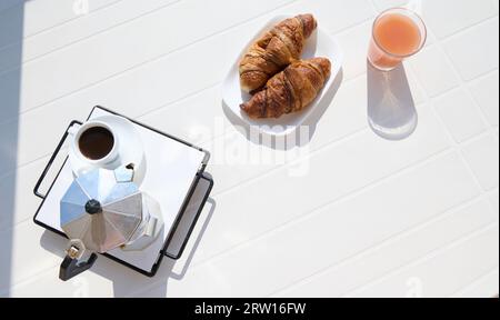 Vue d'en haut à la table blanche avec croissants français fraîchement cuits, verre de jus, une tasse de café expresso infusé dans un percolateur italien ou moka bre Banque D'Images