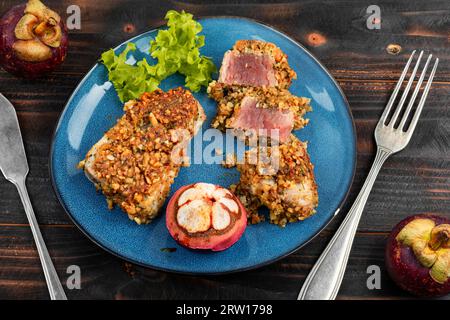 Délicieux steak de thon cuit au four dans une noix avec un mangoustan sur une table en bois sombre. Banque D'Images