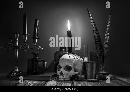 Une image en noir et blanc de bougies dans un candélabre, un crâne avec des gouttes de cire et des objets vintage pour scribes Banque D'Images
