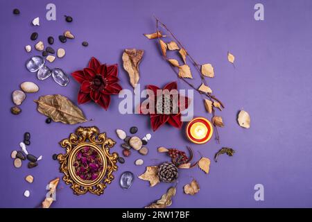 Une nature morte avec quelques fleurs séchées, une bougie allumée, des pierres de différentes couleurs, des feuilles séchées sur une surface lisse violette Banque D'Images