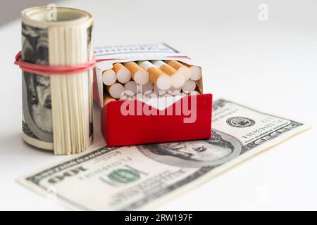 Paquet de cigarettes avec des billets de cent dollars sur un fond bleu. Frais de tabagisme Banque D'Images