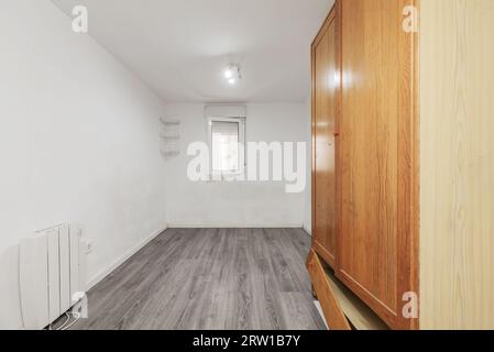 Chambre vide avec une armoire rusée, radiateur électrique, planchers en bois gris, fenêtre en aluminium blanc et murs blancs Banque D'Images